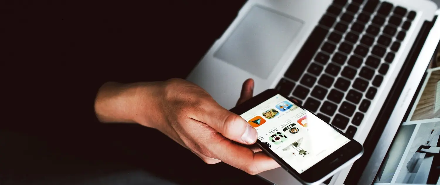 Contact Hand gebruikt smartphone met apps, naast laptop, voor mobiele websites ontwikkeling Totaal Webdesign Bureau intrige.